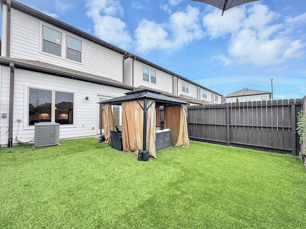 Ein Garten mit überdachter Terrasse, Holzzaun und Rasen.