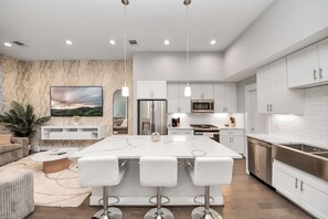 A modern kitchen with white cabinets, a central island with bar stools, stainless steel appliances, and a marble backsplash. - Welcome to Freeman’s House! 
Heart of DTWN HTX ! (Houston)