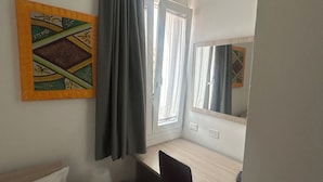 A small, well-lit room with a bed, a desk, a chair, a window with curtains, and a wall-mounted artwork. - Old Town Room 1 (Tortolì)