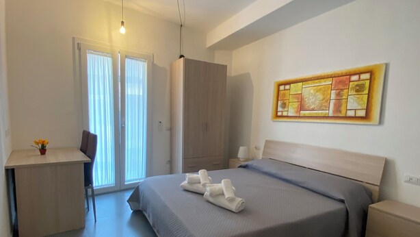 A modern bedroom with a bed, a desk, a wardrobe, and a painting on the wall. - Old Town Room 1 (Tortolì)