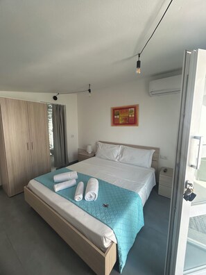 A hotel room with a bed, a wardrobe, a bedside table, an air conditioning unit, and a window. - Old Town Room 1 (Tortolì)