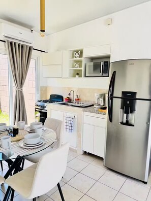 A modern kitchen with a stainless steel refrigerator, microwave, and gas stove. There is a dining table with white chairs and a set of white dishes. - Modern Home in Santa Ana (Santa Ana)