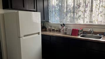 A kitchen with a white refrigerator, dark cabinets, a window with floral curtains, and a stainless steel sink.