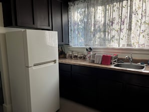 A kitchen with a white refrigerator, dark cabinets, a window with floral curtains, and a stainless steel sink.
