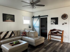 A living room with a sectional sofa, a wooden chair, a ceiling fan, and a painting on the wall.