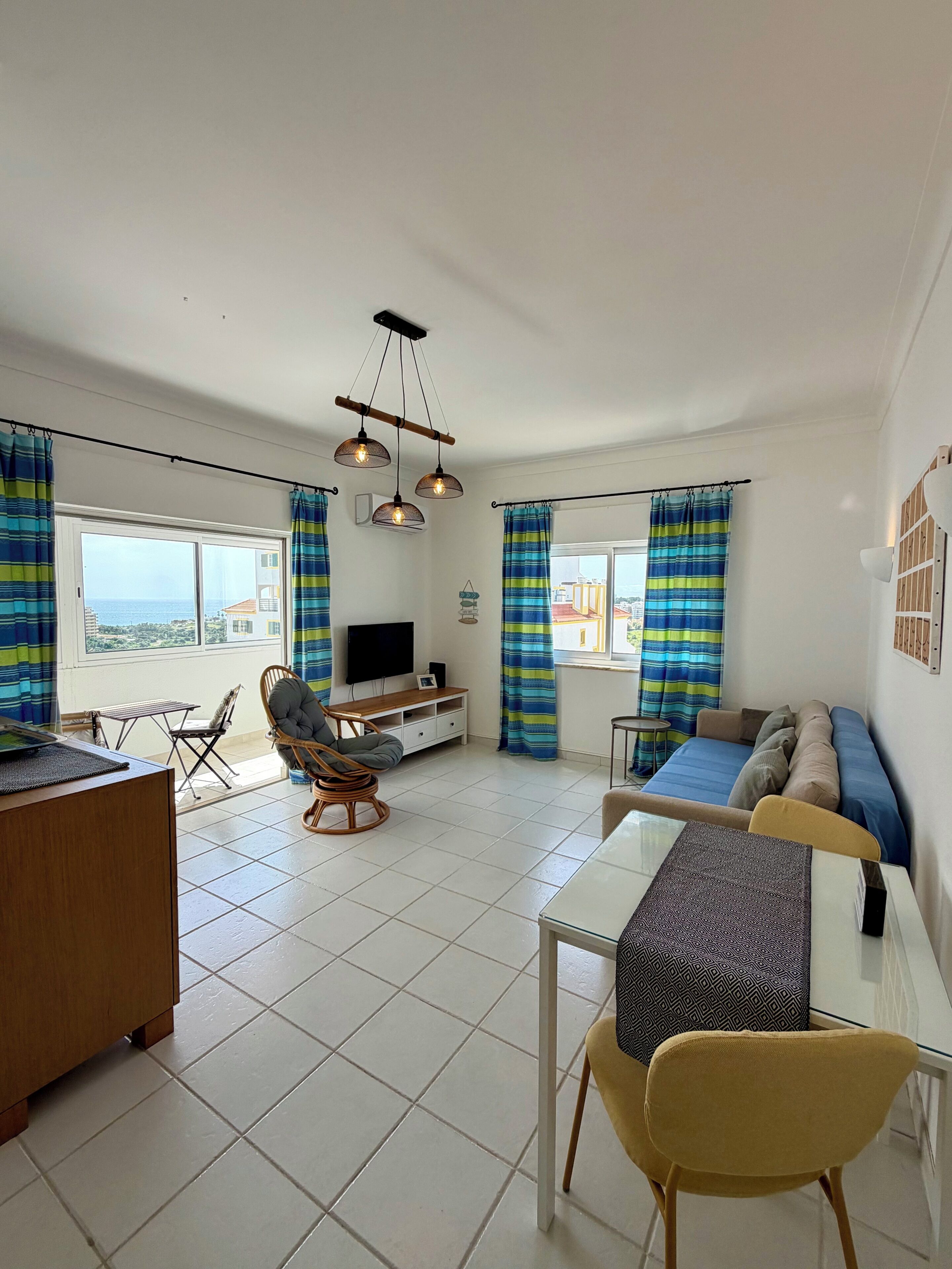 A modern living room with a sofa, dining table, and chairs, a TV, and a view of the sea.