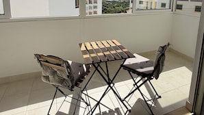 A balcony with a wooden table and chairs, a view of buildings, and a clear sky. - Azul,: A cozy apartment just a few steps from Praia da Rocha (Portimão)