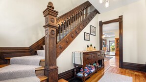 Eine imposante Treppe mit hölzernem Geländer und einer dekorativen Wanduhr, die zu einem Raum mit Holzboden und einem weißen Teppich führt.