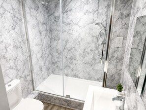 A modern bathroom with a glass-enclosed shower, marble walls, a white sink, and a small potted plant. - Modern 2-Bed Flat Near Donington & Airport (Long Eaton)