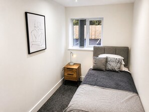 A bedroom with a bed, a bedside table with a lamp, a window, and a framed picture on the wall. - Modern 2-Bed Flat Near Donington & Airport (Long Eaton)