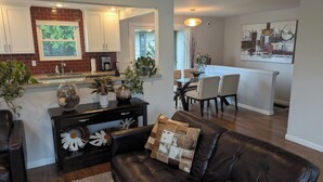 A modern living room with a leather couch, a dining area with chairs, a kitchen with white cabinets, and a dining table. - Exceptional 3 bedroom/3 bath +Office -  Shorewood on the Sound! (Burien)
