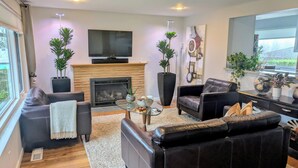 A modern living room with leather sofas, a glass coffee table, a fireplace, and decorative plants. - Exceptional 3 bedroom/3 bath +Office -  Shorewood on the Sound! (Burien)