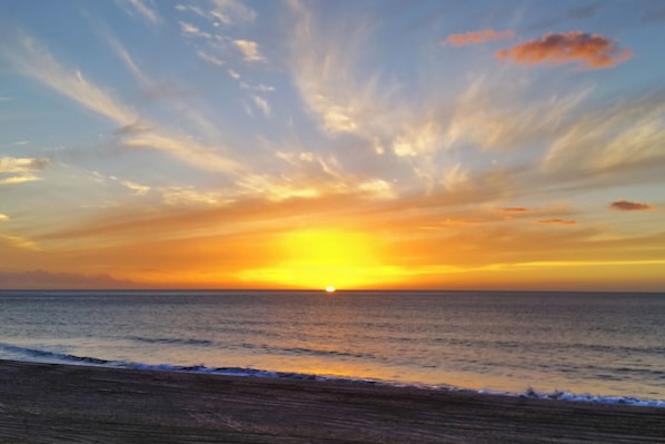 Een zonsondergang boven de oceaan, met een strand op de voorgrond.