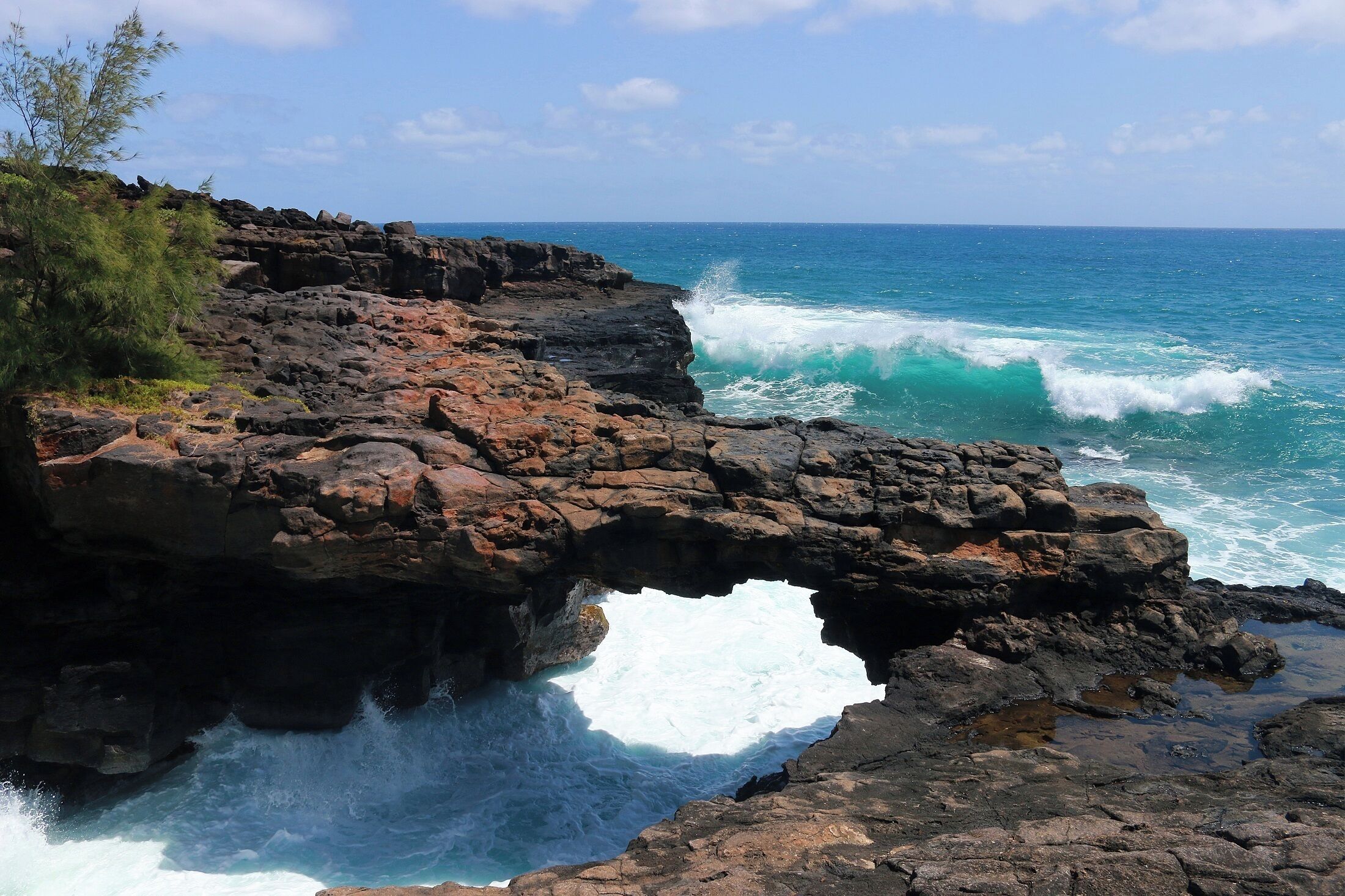 A rocky coastline with a natural arch formation and waves crashing against the rocks.