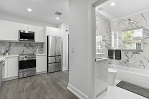 A modern kitchen with stainless steel appliances, a marble backsplash, and a wooden floor.