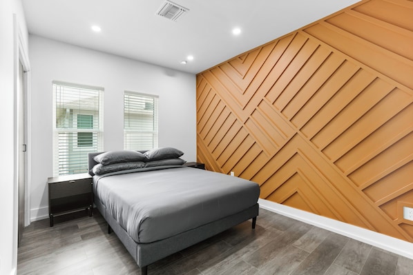 A modern bedroom with a bed, nightstands, and a wooden accent wall.