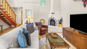 Uma sala de estar com sofá, poltrona, mesa de centro, televisão, lareira e escada.