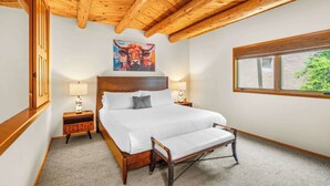 Quarto com teto de madeira, uma cama grande, abajures, um quadro de vaca e janela com vista.