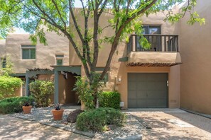 Ein Gebäude mit Balkon, Garage und Garten, einschließlich Kübelpflanzen und einem Baum.