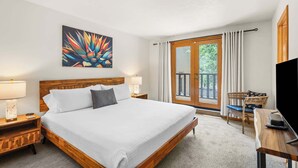 Quarto de hotel com cama, duas mesas de cabeceira, televisão, cadeira e varanda com cortinas.