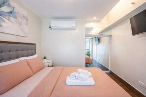 Ein modernes Hotelzimmer mit einem großen Bett, einem kleinen Nachttisch, einem an der Wand montierten Fernseher und einer Klimaanlage.