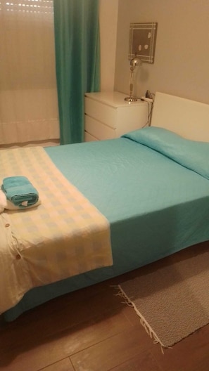 A bedroom with a bed, a bedside table, a lamp, and a window with curtains.