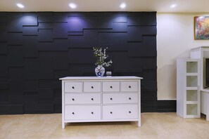A white dresser with multiple drawers, a vase with flowers, and a black wall with geometric patterns. - 2 BR Apt,New Cairo, in small villa guarded 24/7.Walking distance to all you need (Cairo Governorate)