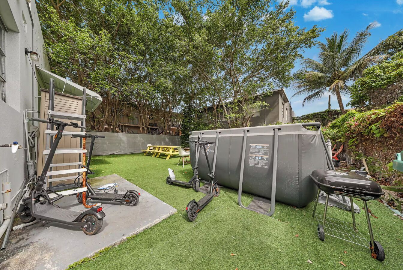 Ein Garten mit Rasenteppich, einem Grill, einem Zelt und zwei Elektrorollern.