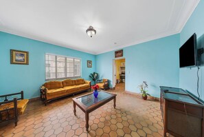 Ein Wohnzimmer mit Sofa, Couchtisch, Fernseher und einer Küche im Hintergrund.