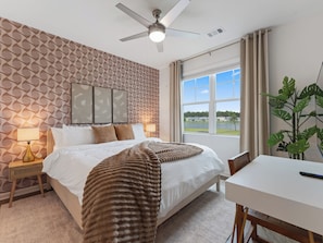 Une chambre à coucher avec un lit, un ventilateur de plafond, une fenêtre donnant sur un beau paysage et une table de chevet avec une lampe.