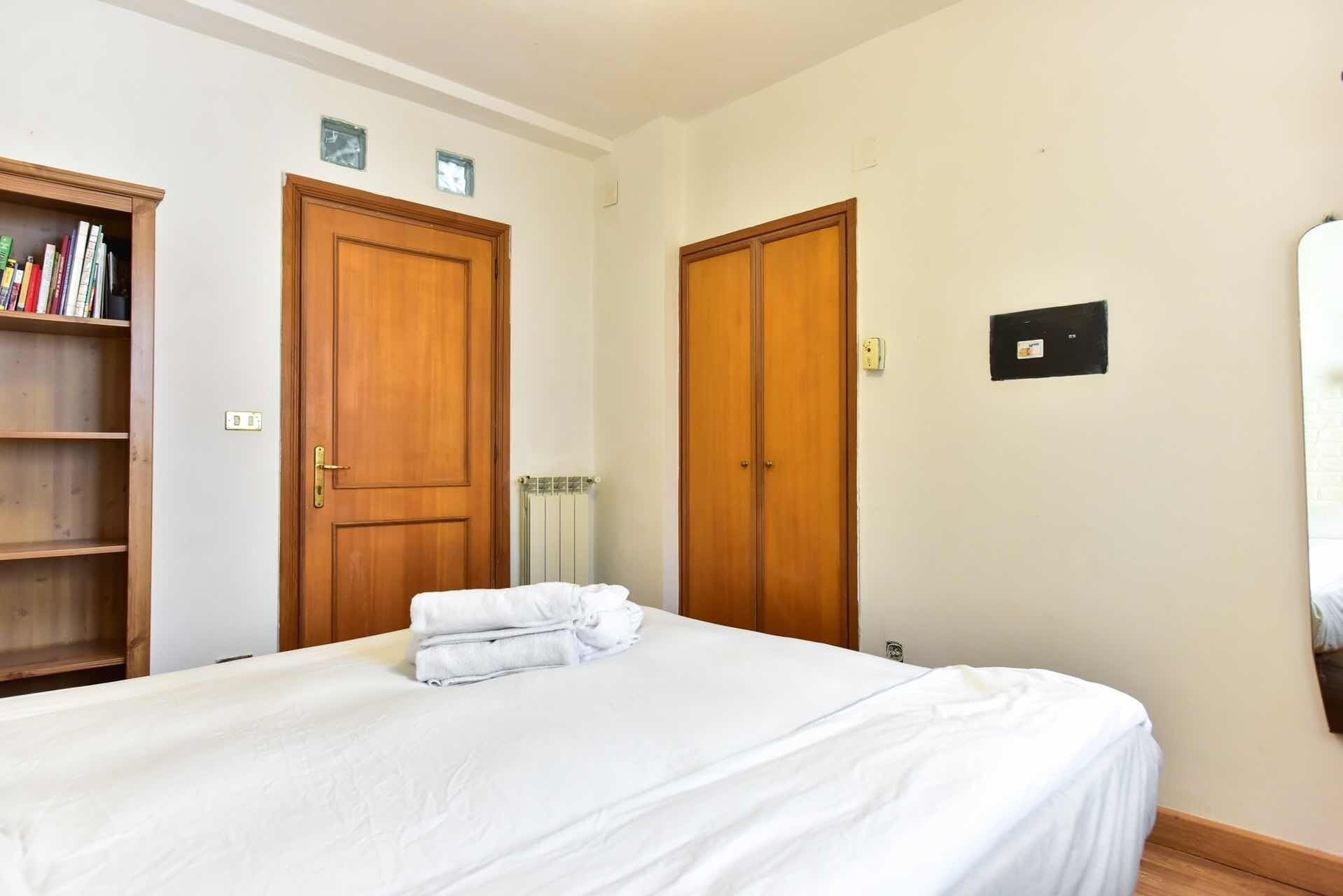 Un dormitorio con una cama, dos puertas de madera, una estantería y un radiador.