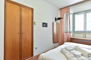 Ein Hotelzimmer mit großem Holzschrank, einem Bett mit weißer Bettwäsche und einem Fenster mit Vorhängen.
