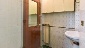 Et badeværelse med dør i træ, hvide flisevægge, en radiator og en hvid vask.