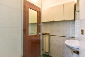 Ein Badezimmer mit Holztür, weißen Fliesen, einem Heizkörper und einem weißen Waschbecken.