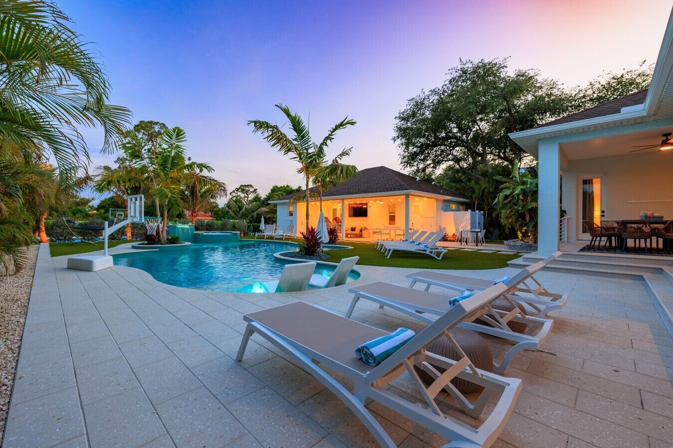A swimming pool with lounge chairs, a house with a patio, and surrounding greenery.