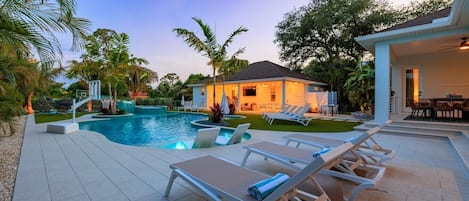 A swimming pool with lounge chairs, a house with a patio, and surrounding greenery.