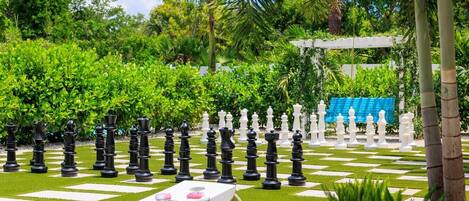 A chessboard set outdoors surrounded by lush greenery and palm trees.