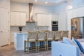 A modern kitchen with white cabinetry, a stainless steel range, and a central island with bar stools. - Luxury Estate w/ Amazing Outdoor Space, Slps 24 (Bradenton)