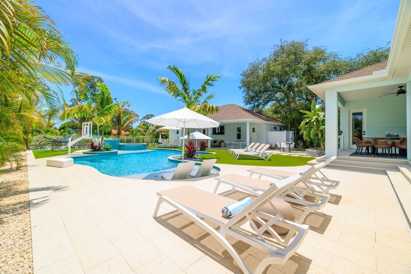 A swimming pool with lounge chairs, a covered patio, and a house with a tiled roof.