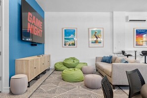 Ein modernes Wohnzimmer mit Fernseher, grünen Sitzsäcken, einer Couch und gerahmten Bildern an der Wand.