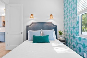 A bed with a headboard, two wall-mounted lights, a potted plant, and a window with blinds. - Luxury Estate w/ Amazing Outdoor Space, Slps 24 (Bradenton)