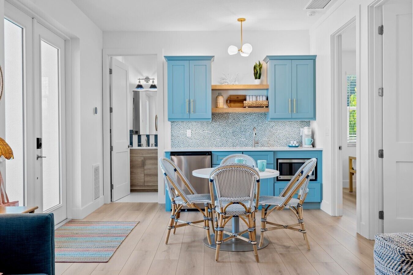 Una cocina moderna con armarios azules, un comedor con sillas de mimbre y una ventana visible.