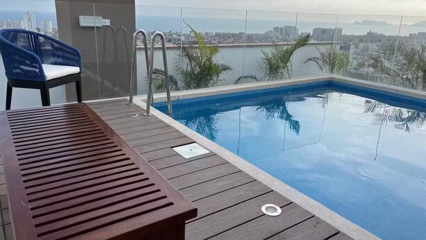 Une piscine sur le toit, avec une terrasse en bois, une chaise bleue et une vue sur le paysage urbain.