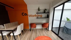 Un espace de bureau moderne avec une table en bois, des chaises blanches et un fauteuil rouge qui apporte une touche de couleur. On peut voir une étagère murale ornée de plantes.