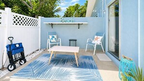 Een terras met een tafel en stoelen, een witte hek en een bordje waarop 'Beach' staat.