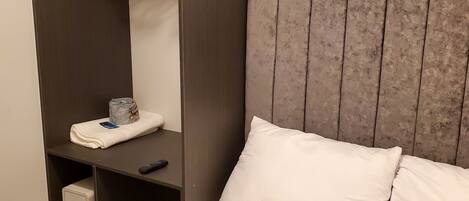 Habitación de hotel con cama, armario empotrado con espacio para colgar, estante con un control remoto y una caja de almacenamiento pequeña.