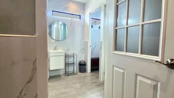 A hallway with a white door, a ceiling fan, and a view into a room with a bathroom.