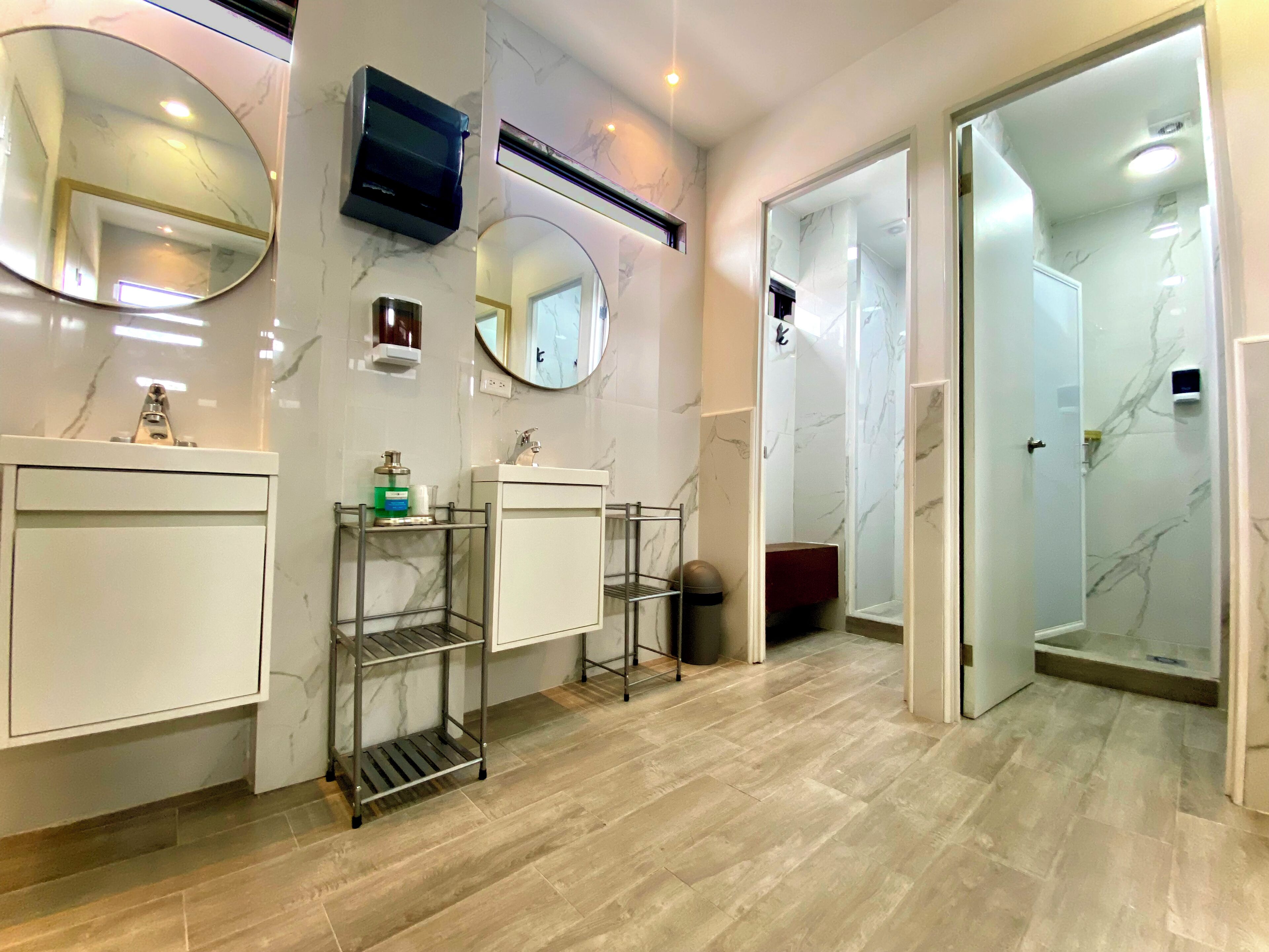 Un baño moderno con paredes de mármol, dos lavamanos, un espejo, un televisor y zona de ducha.