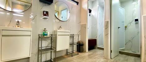 A modern bathroom with marble walls, two sinks, a mirror, a TV, and a shower area.