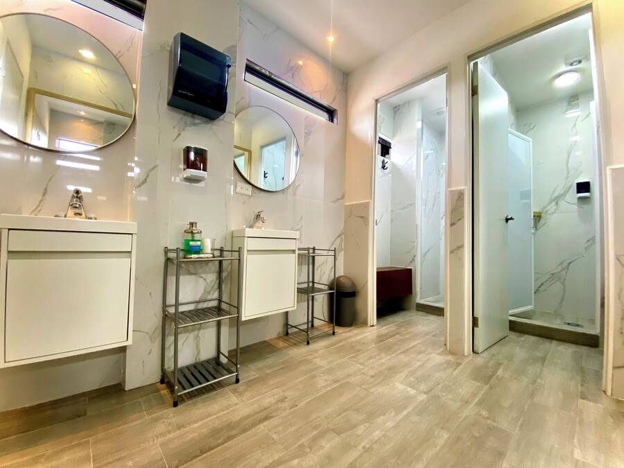 Un baño moderno con paredes de mármol, dos lavamanos, un espejo, un televisor y zona de ducha.